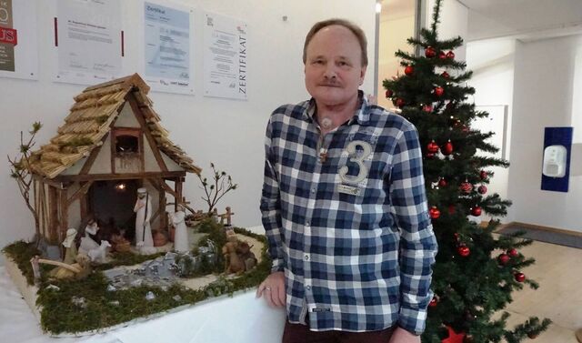 Joachim Tetzlaff steht vor einem Weihnachtsbaum und neben seiner handgefertigten Krippe.