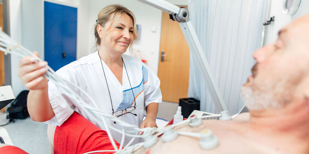 Krankenpflegerin führt bei einem Patienten ein EKG durch.