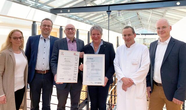 Einige Männer und Frauen halten zwei Bildrahmen mit Zertifikaten in der Hand. 