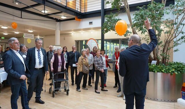Herr Schaufenberg führt eine Gruppe von ca. 20 Personen durch die Niederrhein Klinik. Er steht vor einem großen Pflanzkorb und zeigt erklärend nach oben.